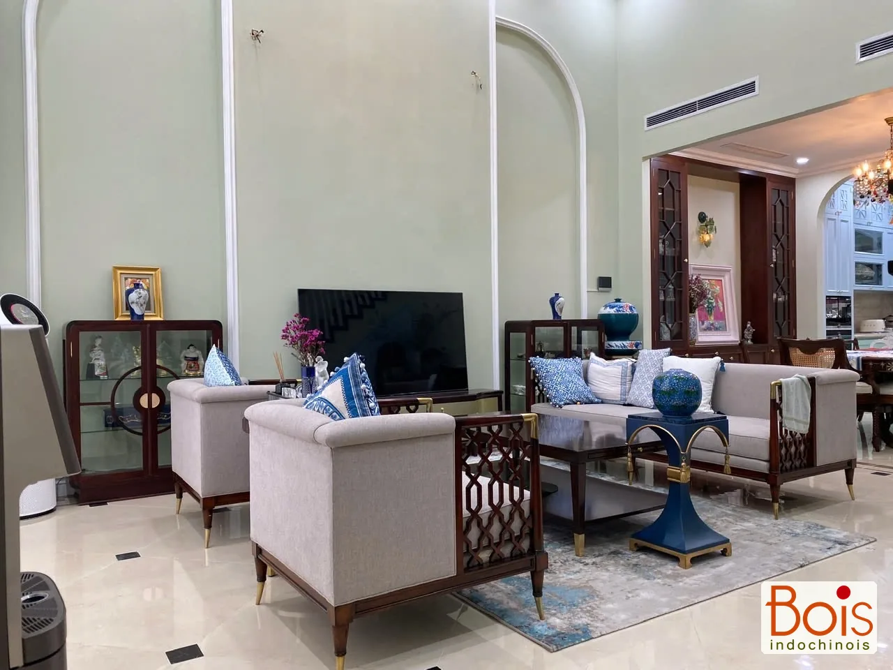 Ảnh thực tế — Nhóm sofa sáng màu trên khung gỗ trầm; khoảng mở phía sau nối về khu ăn.