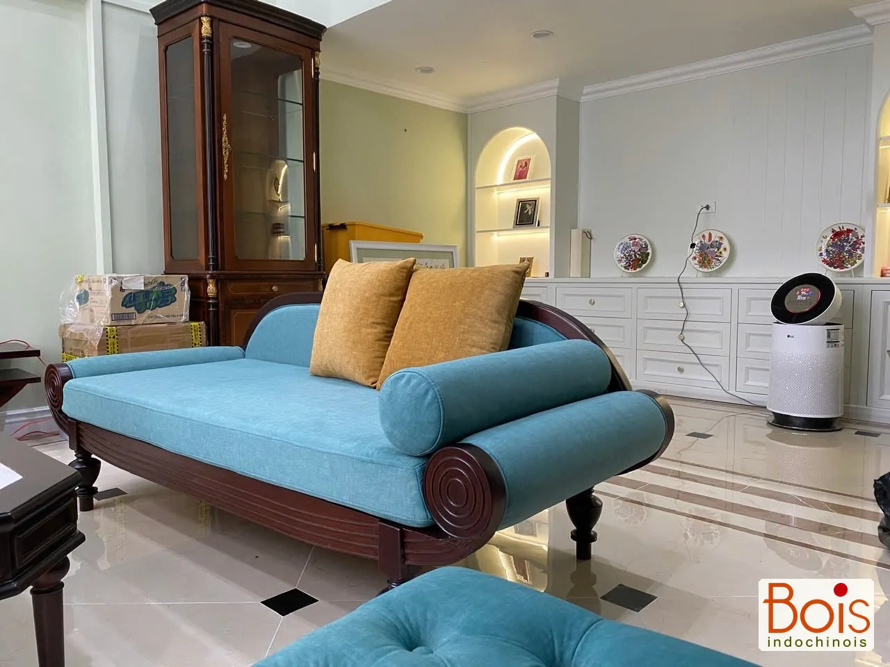Ảnh thực tế — Màu bọc xanh, gối vàng và đường cong của khung gỗ tạo sắc thái riêng cho khu sinh hoạt chung.